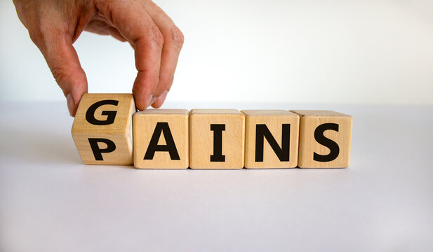 Gains and pains symbol. Businessman turns wooden cubes, changes word pains to gains. Beautiful white background. Business, pains and gains concept. Copy space.