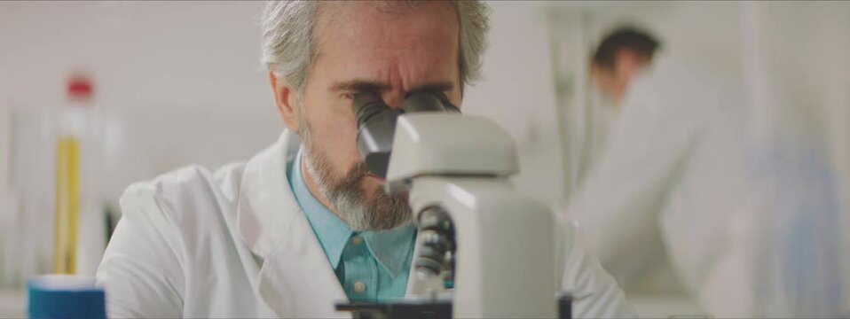 Man in lab coat using microscope to examine observed material. Working in factory laboratory concept.