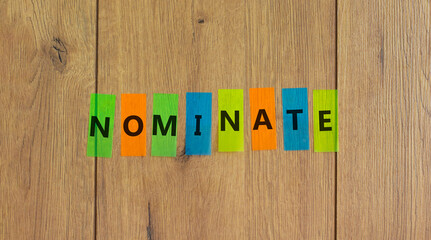 Nominate symbol. Concept word 'nominate' on colored papers on a beautiful wooden background, copy...
