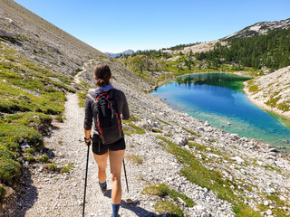 Female hiker hiking along crystal clear mountain lake.