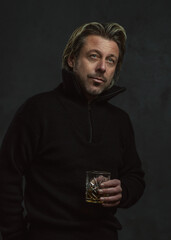 Blonde man in black woolen sweater holding glass of whiskey.