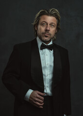 Serious blonde man with stubble beard in tuxedo.