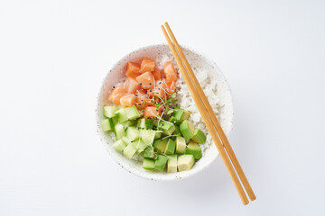 Salmon poke bowl with fresh fish, rice, cucumber, avocado with black and white sesame. White table....