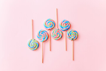 Colorful lollipops swirls on sticks. Striped spiral multicolored candy on pink background, top view