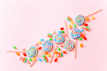 Colorful lollipops swirls on sticks. Striped spiral multicolored candy on pink background, top view