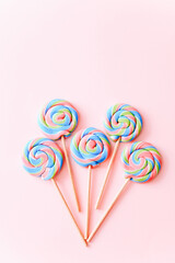 Colorful lollipops swirls on sticks in row. Striped spiral multicolored candy on pink background, top view