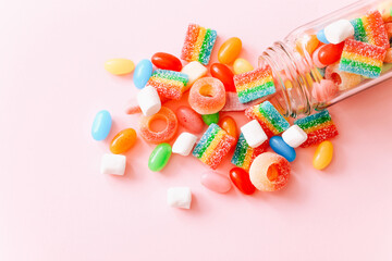 Mixed colorful candies scattered from glass bottle on pink background. Close up