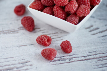 Ripe raspberry in small white bowl on white a wooden background.