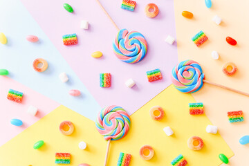 Colorful lollipops swirls on sticks and jelly candies on colorful background, top view