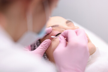 Obraz na płótnie Canvas Beautician wiping cream on clients eyelid with cotton swab closeup