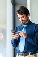 Businessman smiling, holding and looking at his smartphone. Happy successful male portrait 
