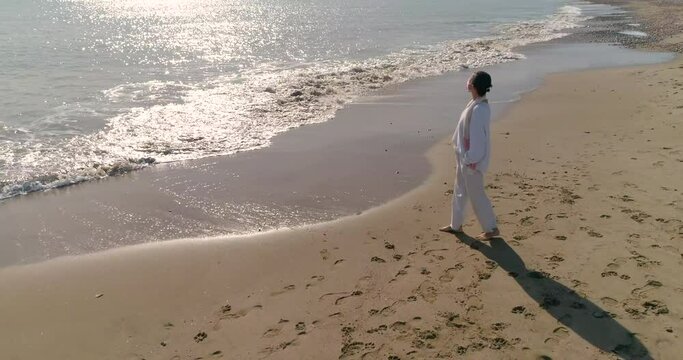 Mujer  senior con mascara covid-19 paseando por la playa sola vestida de blanco