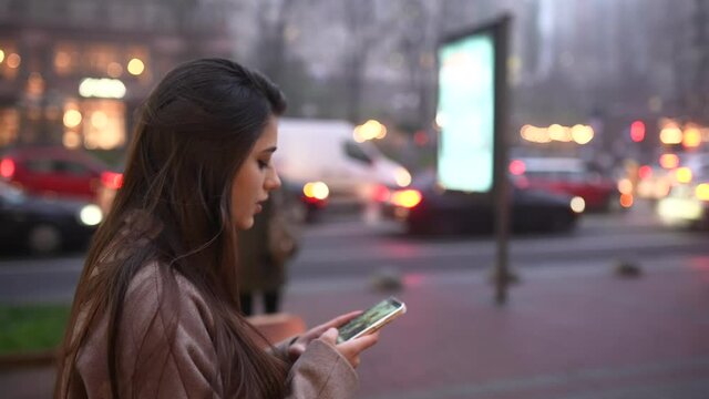 Young woman walking down the street and typing in her mobile phone.