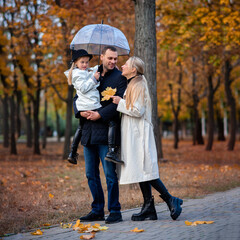 Fototapeta premium Happy family on a walk in the park under an umbrella