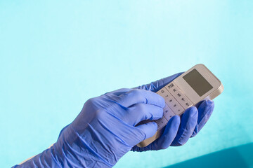 hand in a blue latex glove prints something on a white calculator on a blue background. Copy of space.