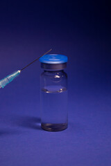 Vaccine bottle phial with no label, medical syringe injection needle. isolated on blue background....