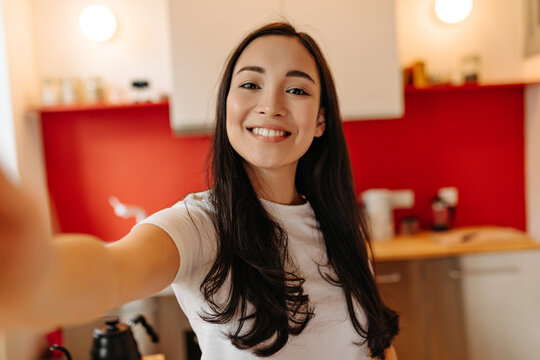 Woman in great mood takes selfie in kitchen. Portrait of brown-eyed girl
