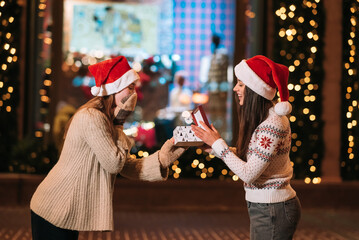 The girl gives a gift to her female friend on the street.
