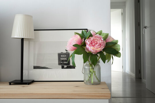 Nordic style auxiliary furniture with a bouquet of peonies, a table lamp and a painting with a black and white photography. Simple and romantic decoration