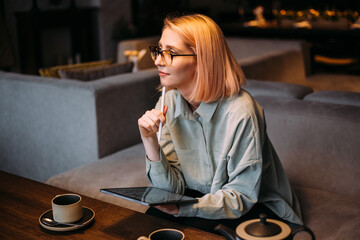 Young creative designer woman in glasses holding stylus pen drawing on digital tablet while sitting...