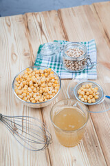 Top view of a wooden table with a solution of Aquafaba made from boiled chickpeas. Boiled and dry chickpeas, a whisk for whipping and a decoction of Aquafaba on the table.