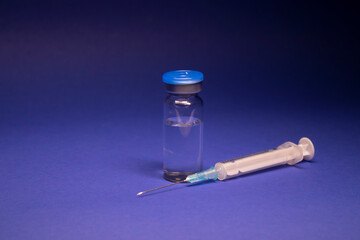 Vaccine bottle phial with no label, medical syringe injection needle. isolated on blue background....