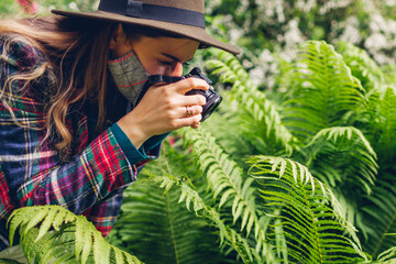 Woman photographer takes pictures on digital camera in summer park wearing mask. Coronavirus...