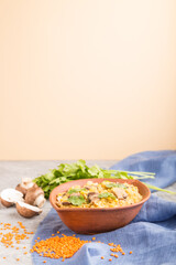 Lentils porridge with champignons. and coriander in a clay bowl on a gray and orange background. Side view, selective focus, copy space.