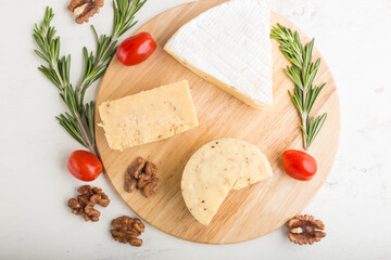 Cheddar and various types of cheese with rosemary and tomatoes on wooden board on a white background . Top view.