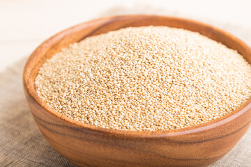 Wooden bowl with raw white quinoa seeds on a white wooden background. Side view, selective focus.
