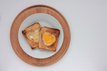 Toast bread with fried egg in a heart shaped hole on plate on white background. Creative Valentine's day or Mothers day breakfast idea