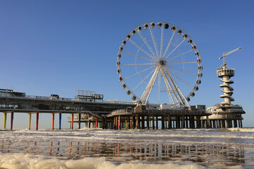 Ferris wheel on De Pier in The Hague Scheveningen on a windy winter day with blue sky and people at the beach, the Netherlands, Europe