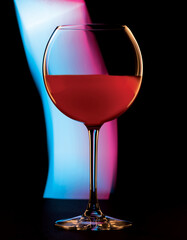 glass cocktail glass with red liquid on black background. Red-blue ray of light in the background.