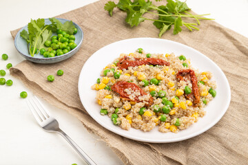 Quinoa porridge with green pea, corn and dried tomatoes on ceramic plate on a white wooden background. Side view.