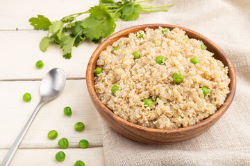 Quinoa porridge with green pea in wooden bowl on a white wooden background. Side view.