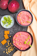 Hummus with beet and microgreen basil sprouts in wooden bowl on a black concrete background. Top view, close up.