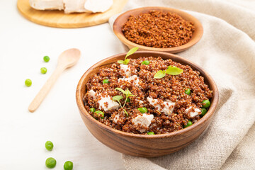 Quinoa porridge with green pea and chicken in wooden bowl on a white wooden background. Side view.