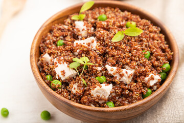 Quinoa porridge with green pea and chicken in wooden bowl on a white wooden background. Side view, selective focus.