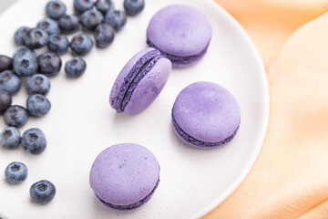Purple macarons or macaroons cakes with blueberries on white ceramic plate on a gray concrete background. Top view, selective focus.
