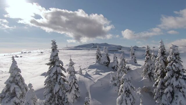 DRONE: Spectacular aerial shot of snow covered mountain range and cottages of Velika Planina, Slovenia. Flying away from a tourist mountain village full of empty wooden huts on a sunny winter day.