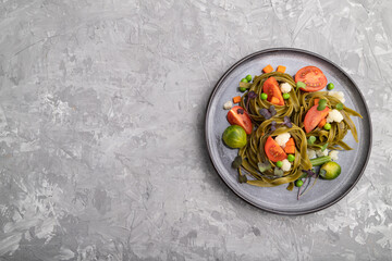 Tagliatelle green spinach pasta with tomato, pea and microgreen sprouts on a gray concrete background. Top view, copy space.