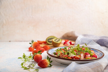 Vegetarian fruits and vegetables salad of strawberry, kiwi, tomatoes, microgreen sprouts on white concrete background. Side view, selective focus, copy space.