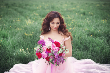 Beautiful bride in pink dress sitting on the grass with her bouquet. A destination summer wedding, romantic country ceremony.