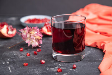 Glass of pomegranate juice on a black concrete background. Side view, selective focus.