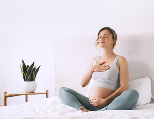 Pregnant woman in lotus pose doing meditation or breathing exercises for healthy pregnancy and...