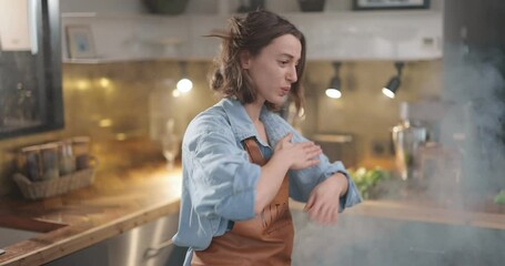 Tired housewife hurries on the kitchen with a smoke from burning food. Exhaustion from household chores and home routine concept - Powered by Adobe