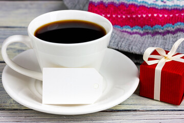 A cup of coffee, a red gift and a blank paper tag on a light table. Gift for a loved one, surprise