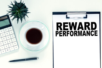 REWARD PERFORMANCE is written on a notepad on an office desk with office accessories. Busiess concept.