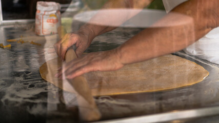 Signora esperta nel lavorare la pasta sfoglia prepara le tagliatelle fatte a mano con matterello e farina