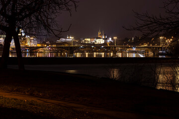 .panoramic view of Prague Castle and St. Vitus Cathedral and the Vltava River and street lights on bridges at night in the center of Prague